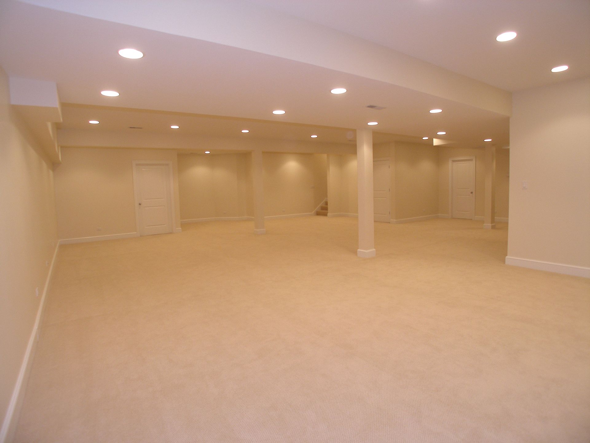 An empty basement with beige carpet and white walls.