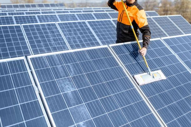 A Man Is Cleaning Solar Panels on A Roof with A Mop