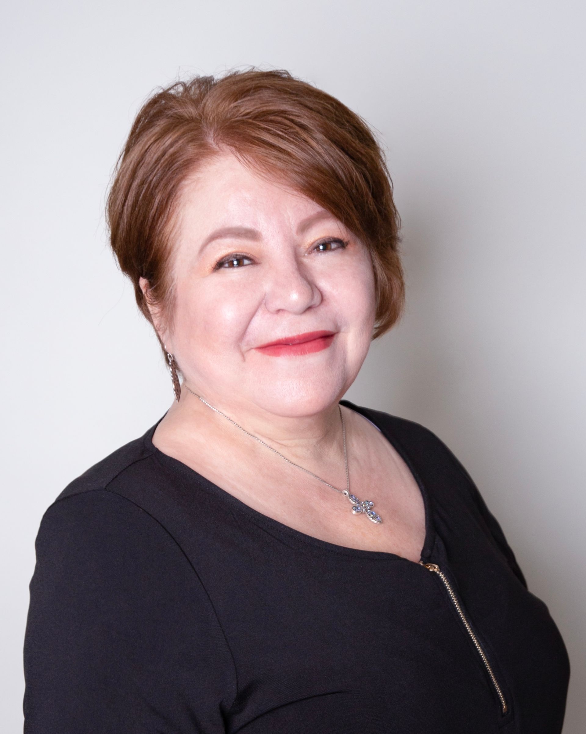 A woman is sitting at a desk with a laptop and a vase of flowers.