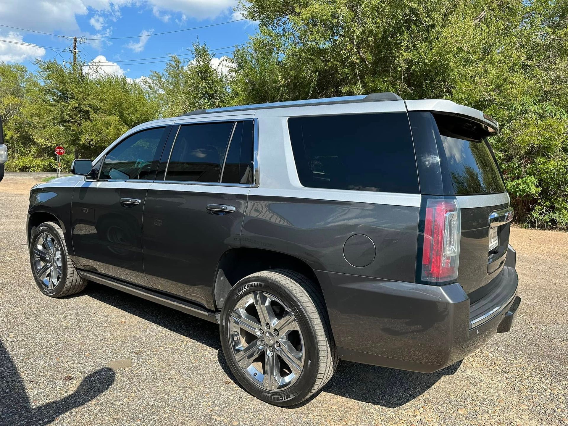 A charcoal grey and silver two-tone SUV parked on a gravel lot with trees in the background.