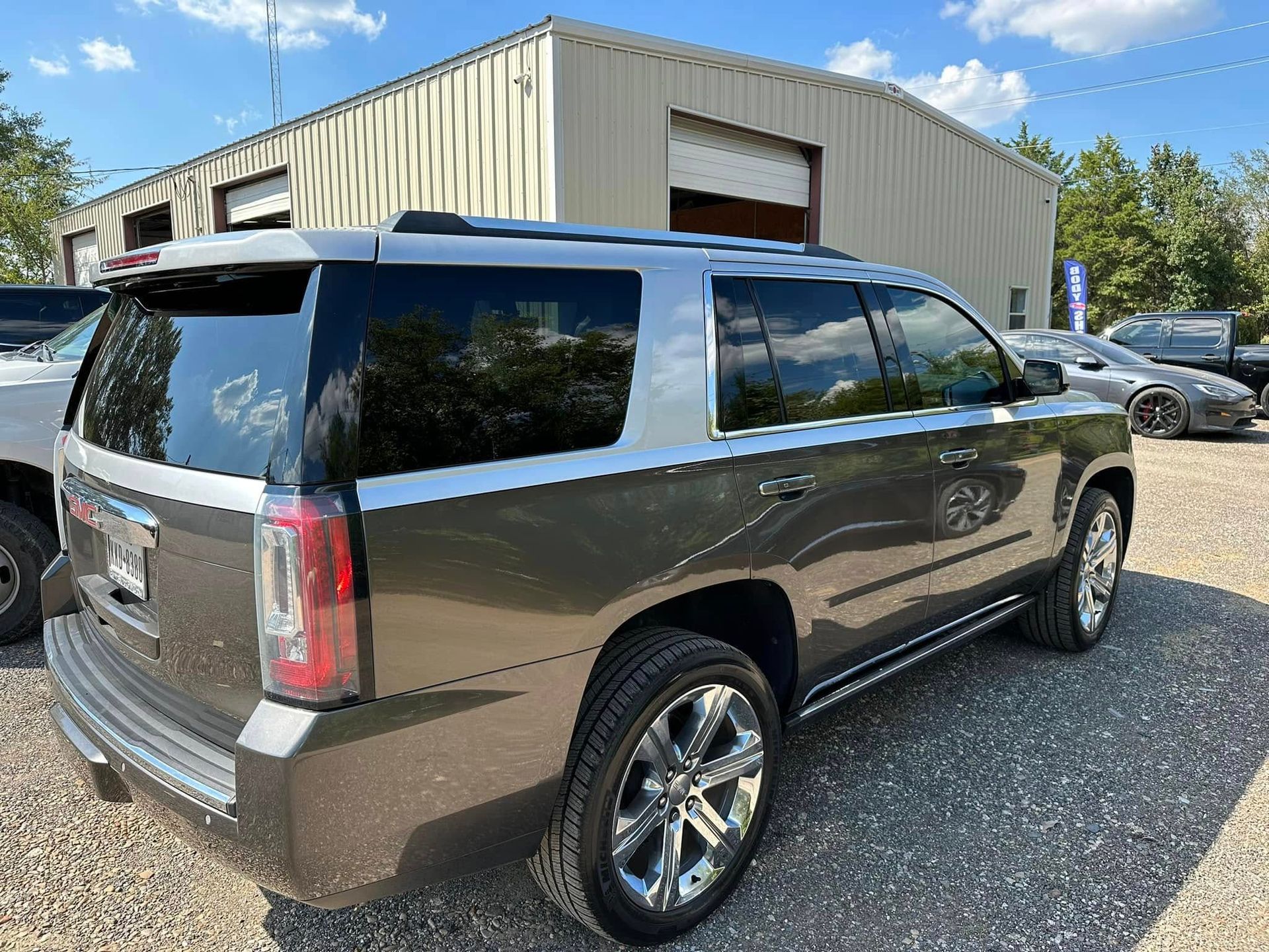 A metallic brown GMC Yukon SUV parked on a gravel lot in front of a metal-sided building under a blue sky.