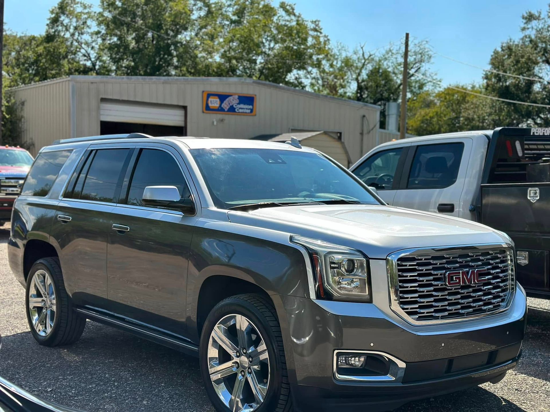 A gray GMC Yukon SUV parked on a gravel lot in front of a building on a sunny day.
