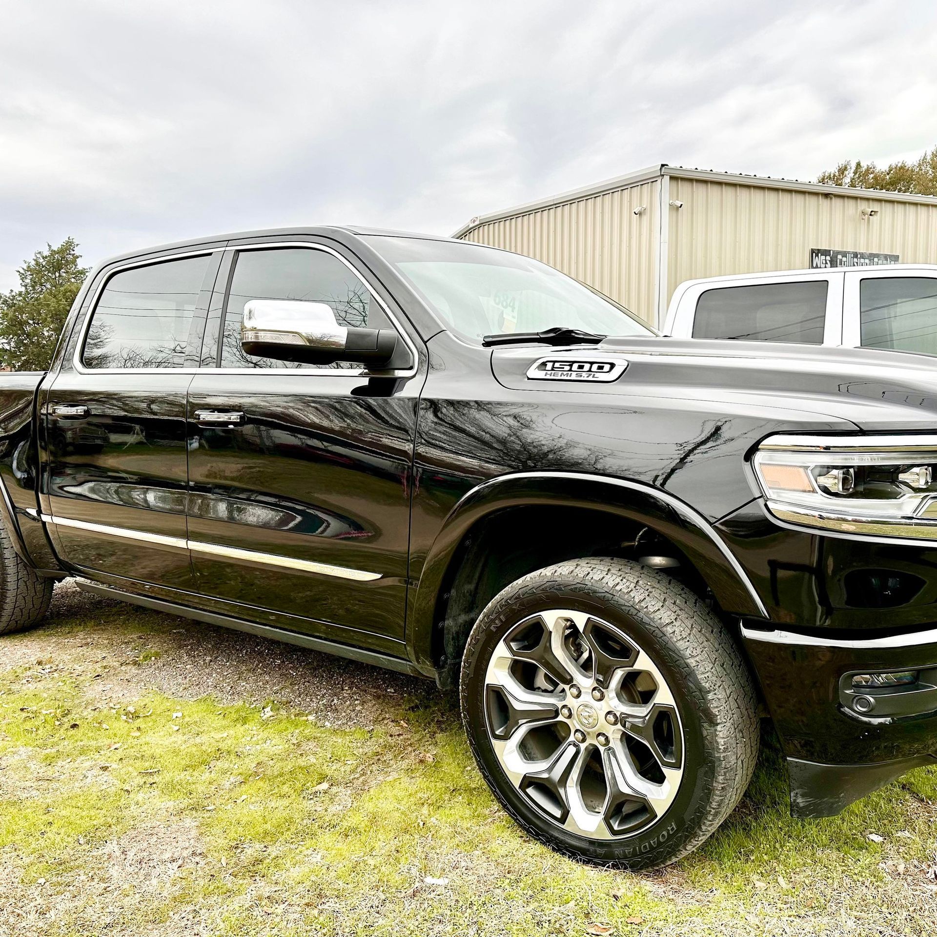 A black Ram 1500 crew cab pickup truck parked on gravel in front of a metal building.