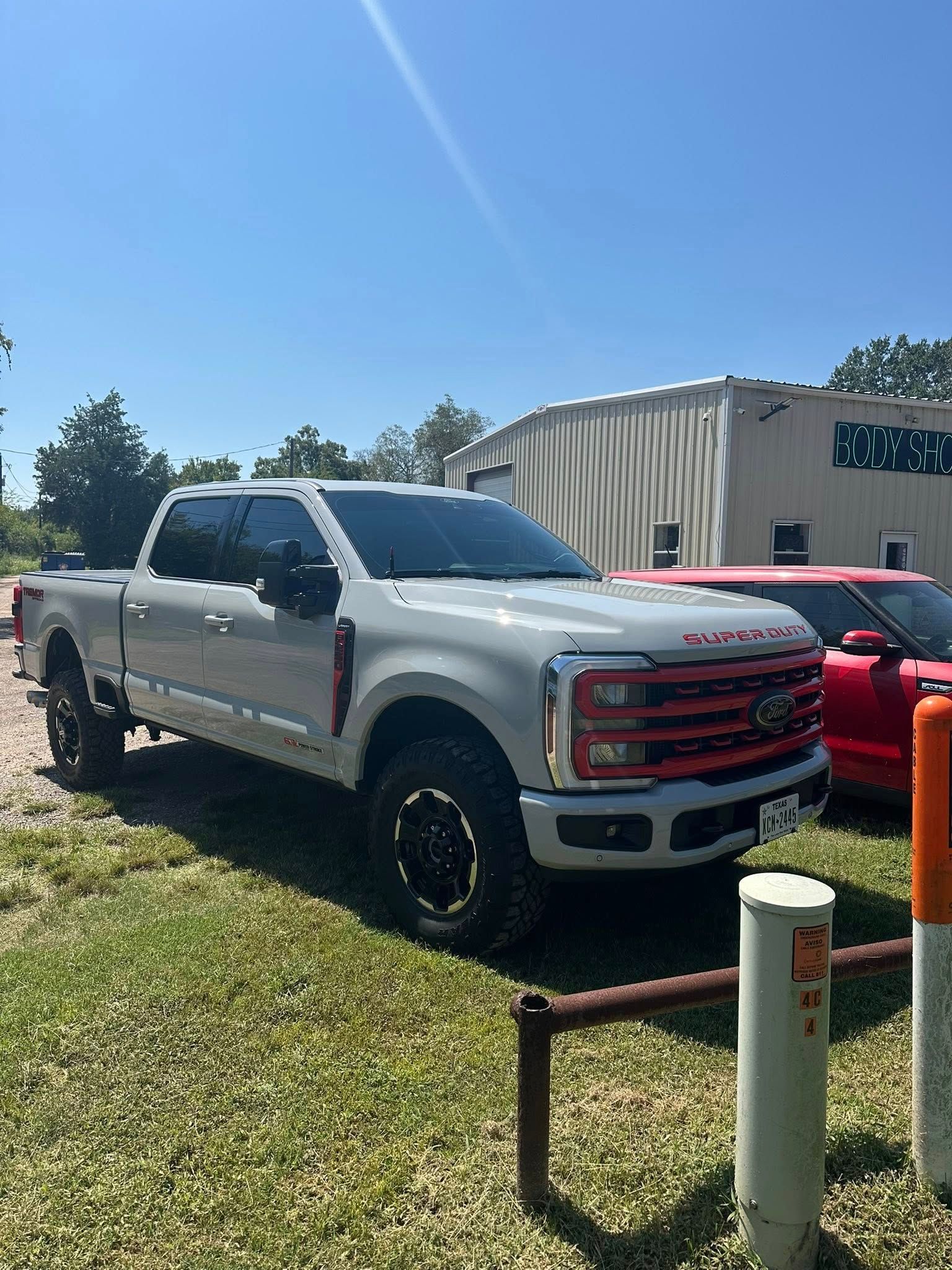 A light gray Ford Super Duty pickup truck with a red grille parked in a grassy lot on a sunny day.