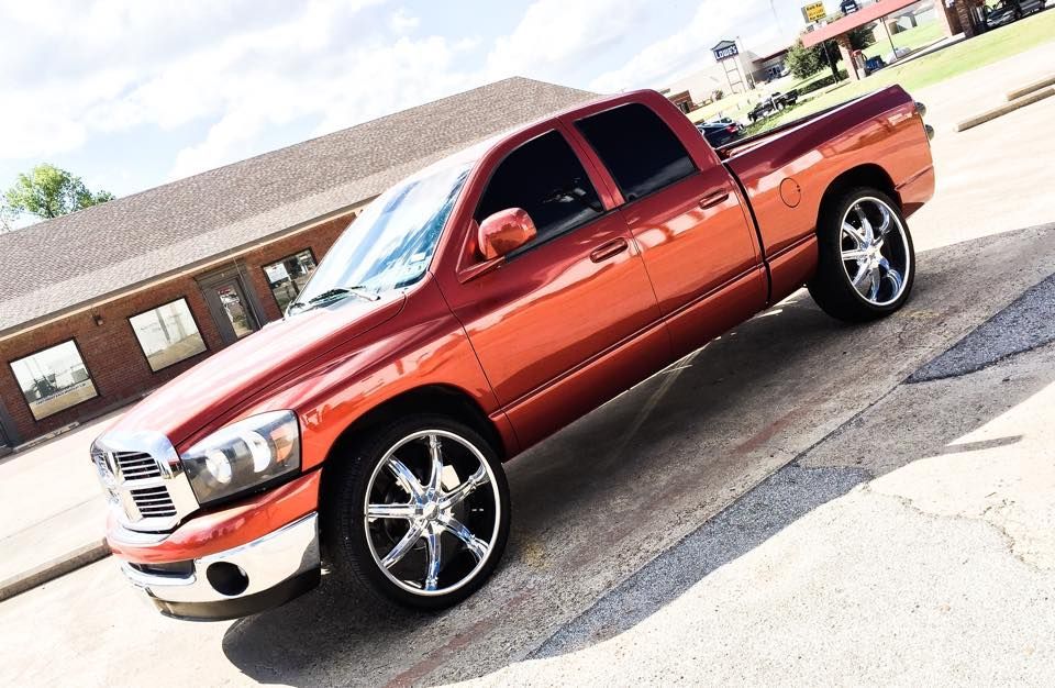 A bright orange Dodge Ram pickup truck parked on a concrete lot, featuring large aftermarket chrome wheels.