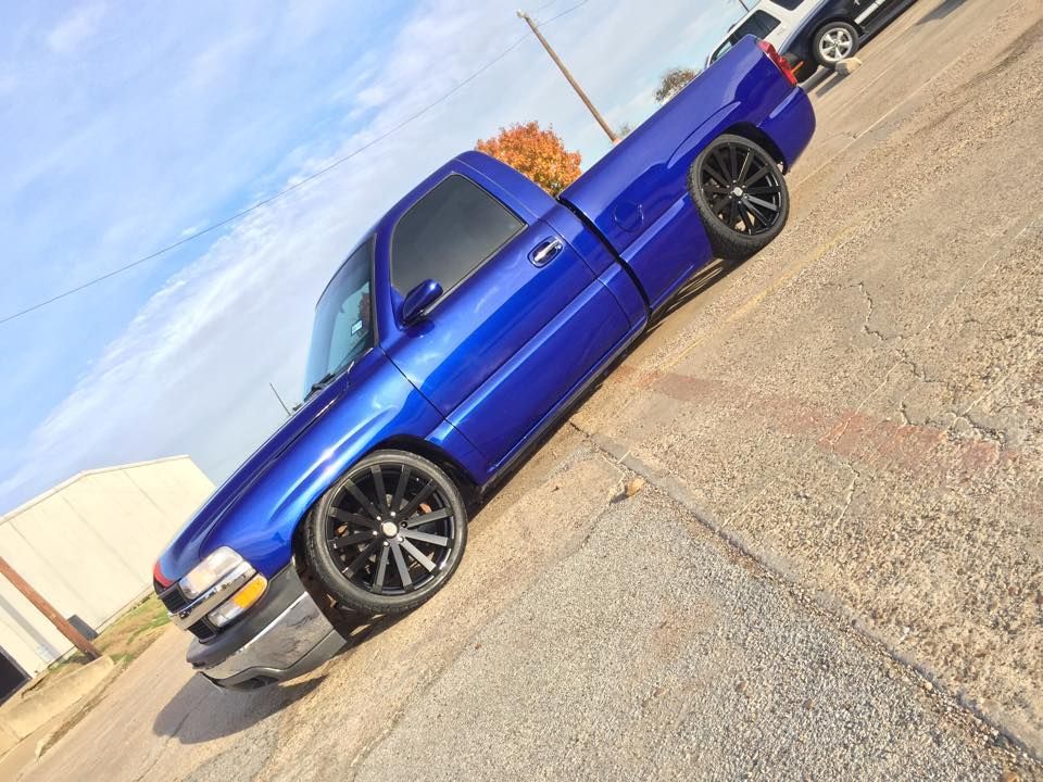 A lowered, bright blue pickup truck with black custom rims parked on a paved lot under a blue sky.
