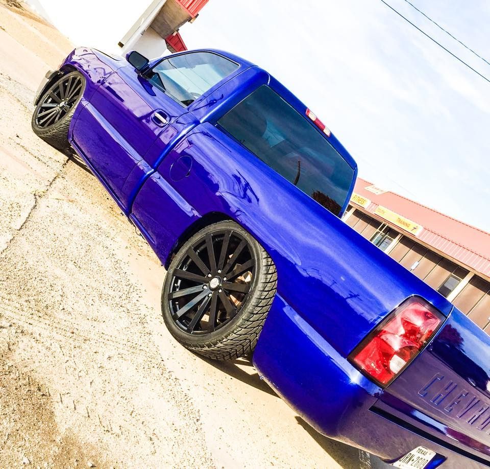 A vibrant, metallic blue Chevrolet pickup truck parked on an angled concrete lot with black custom wheels.