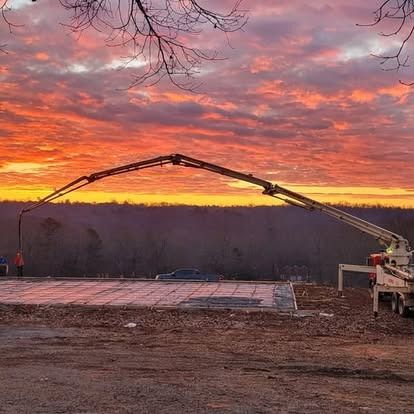 A concrete pump is pouring concrete on a construction site at sunset.