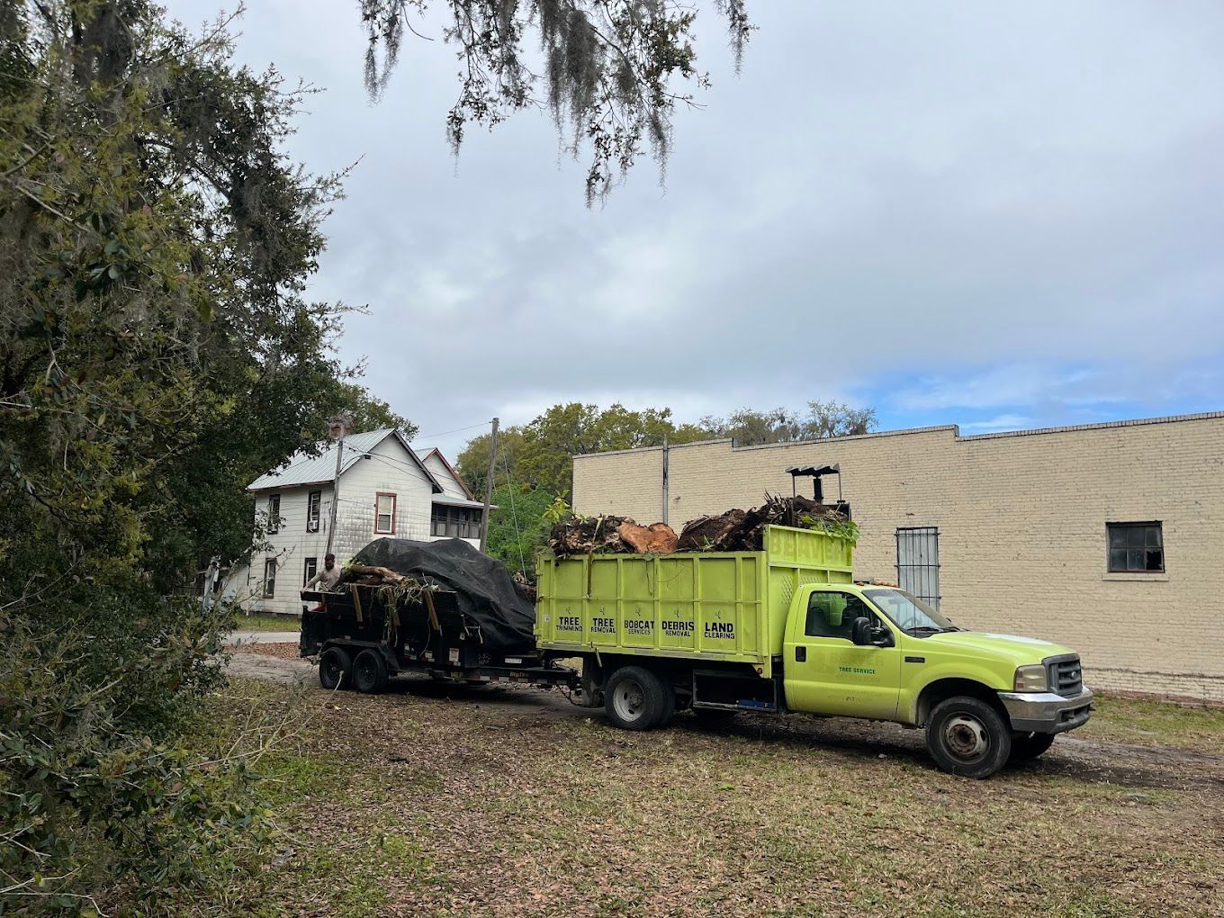 A yellow truck with a trailer full of wood is parked in front of a building.