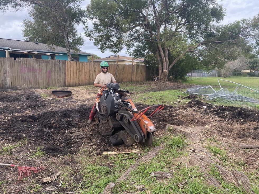 A man is standing next to a tree stump grinder in a field.