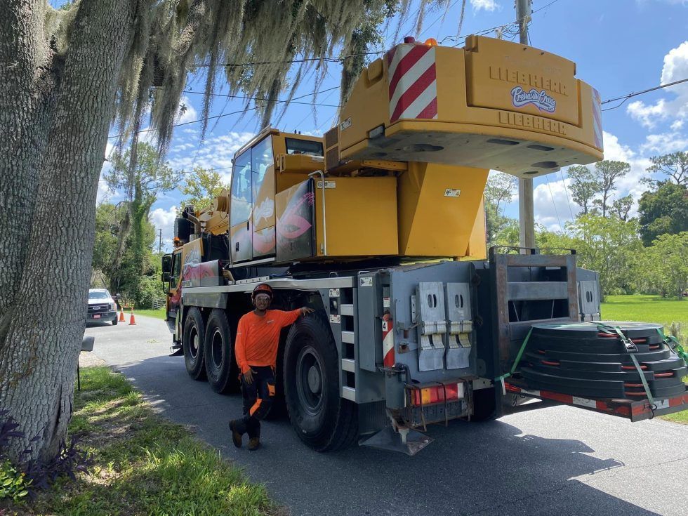 A man is standing next to a large yellow crane on the side of the road.