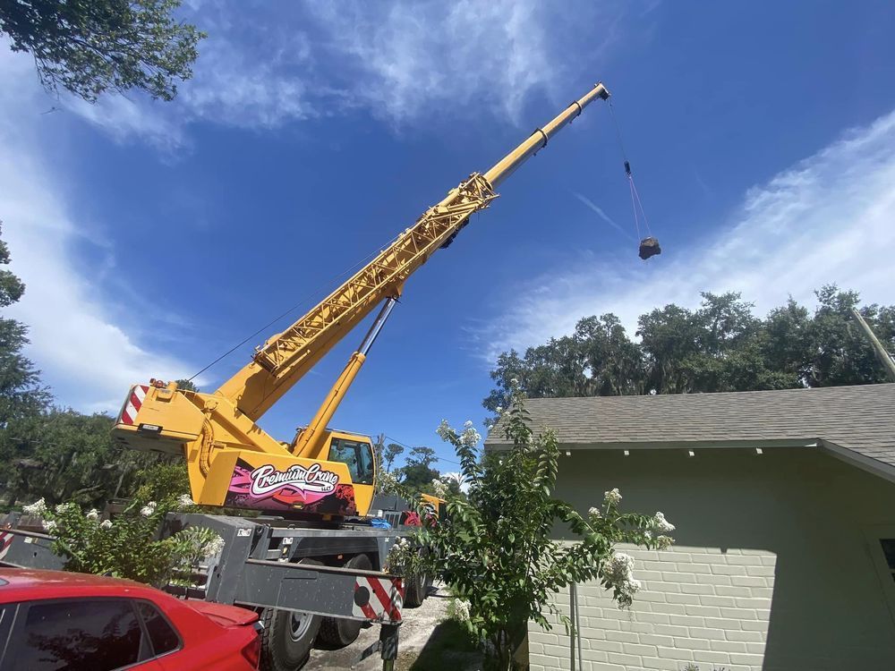 A yellow crane is lifting a red car from the roof of a house.