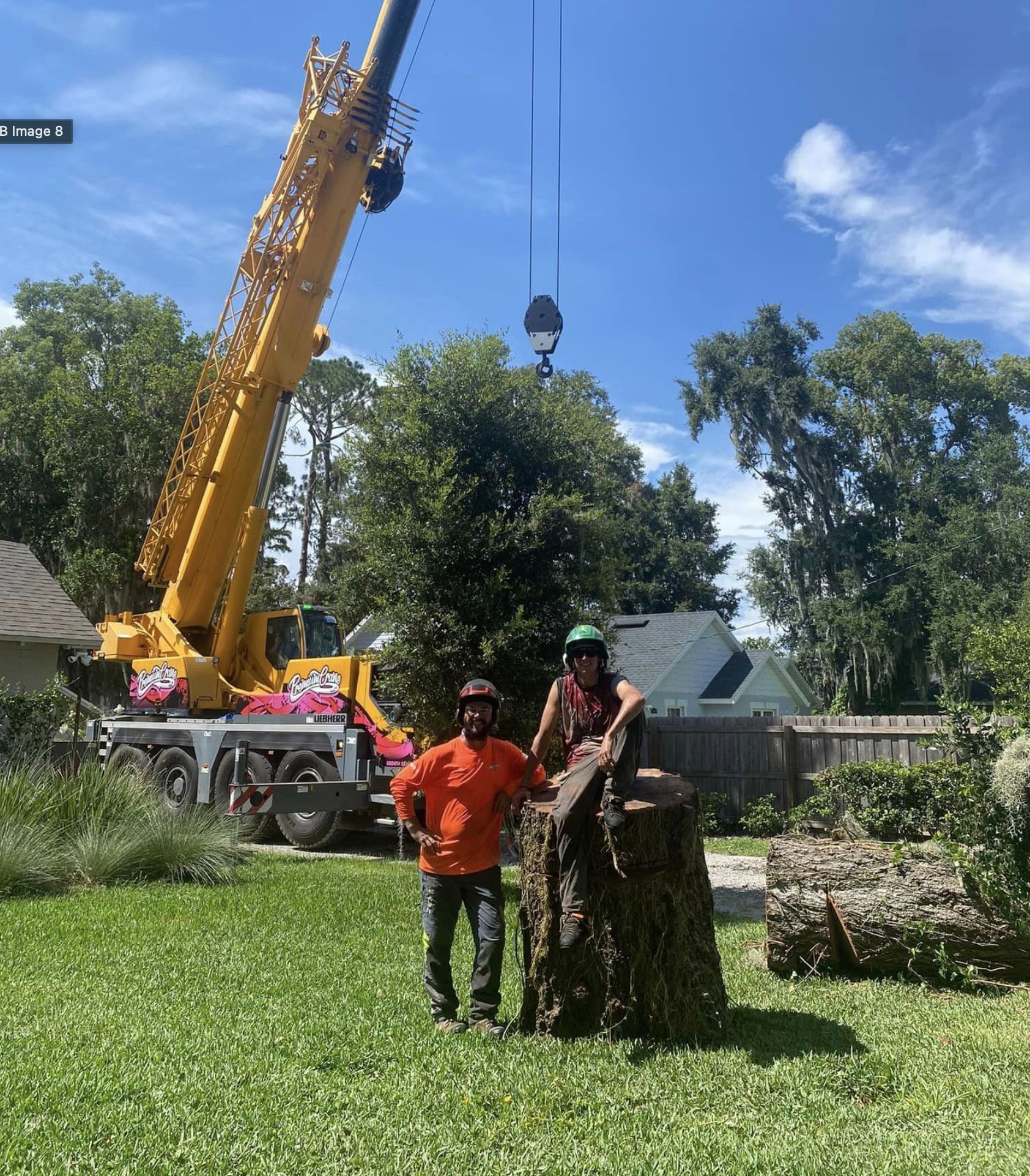 Two men are standing next to a tree stump in front of a crane.