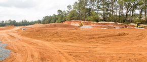 A construction site with a lot of dirt and trees in the background.
