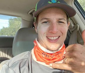 A man wearing a hat and a bandana is giving a thumbs up in a car.