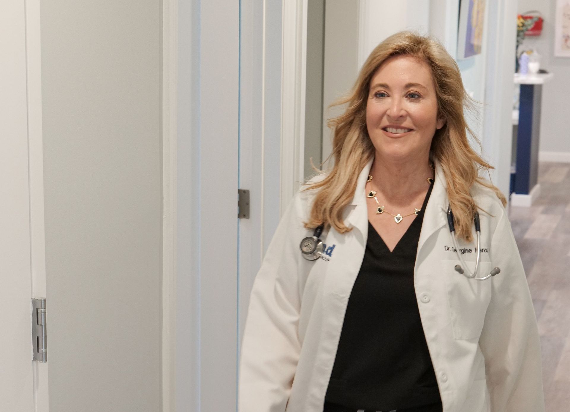 A woman physician in a lab coat is walking down a hallway.