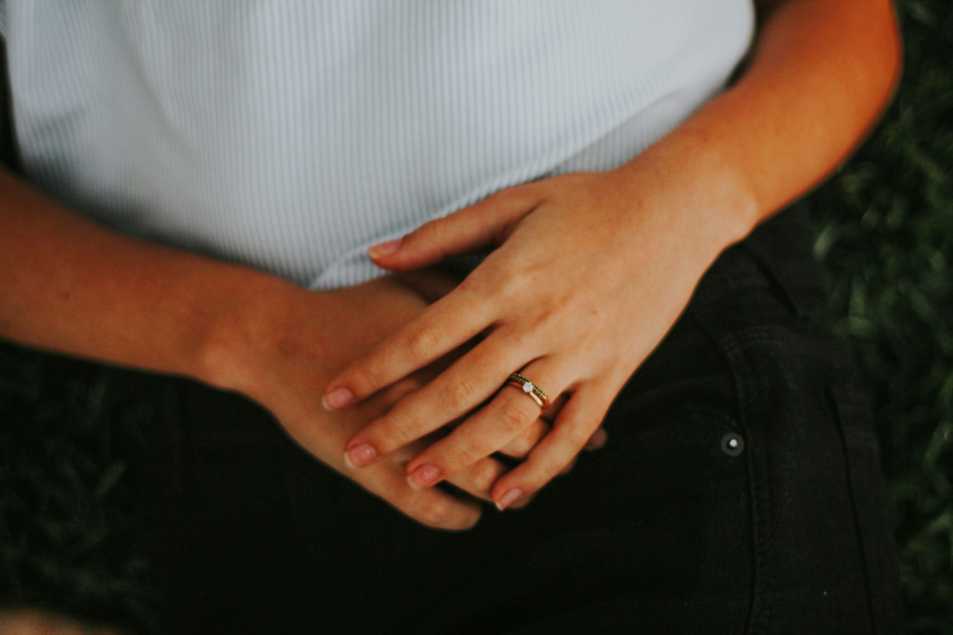 Two hands clasped at a waist, one with a ring, against a dark shirt and pants.