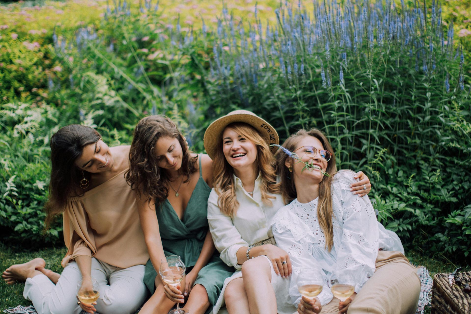 Four friends sitting together in a garden, smiling and hugging among tall purple flowers