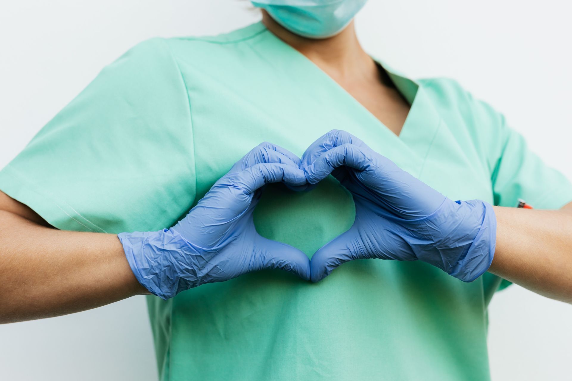 Gloved hands forming a heart gesture over teal medical scrubs