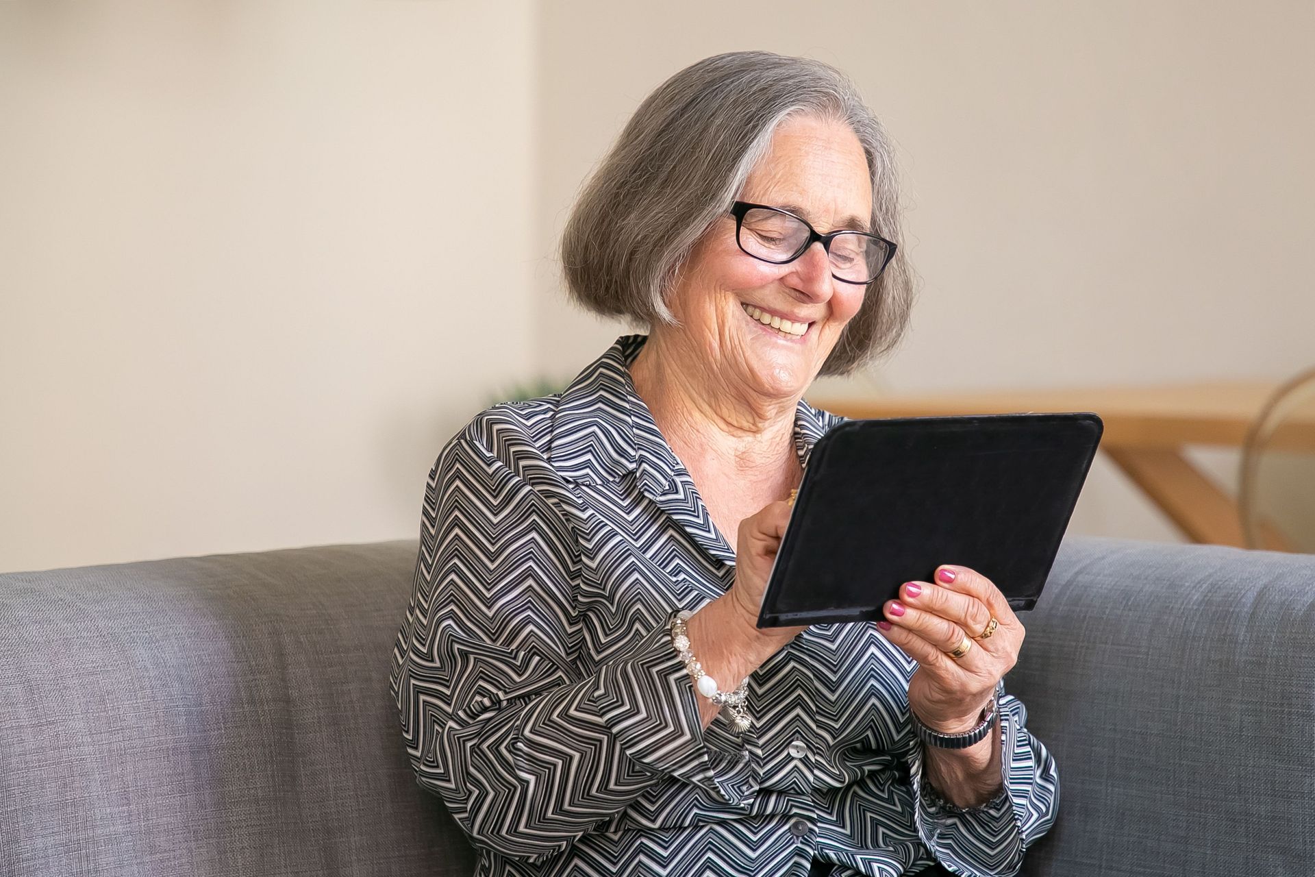 Smiling woman on a couch using a tablet in a bright living room
