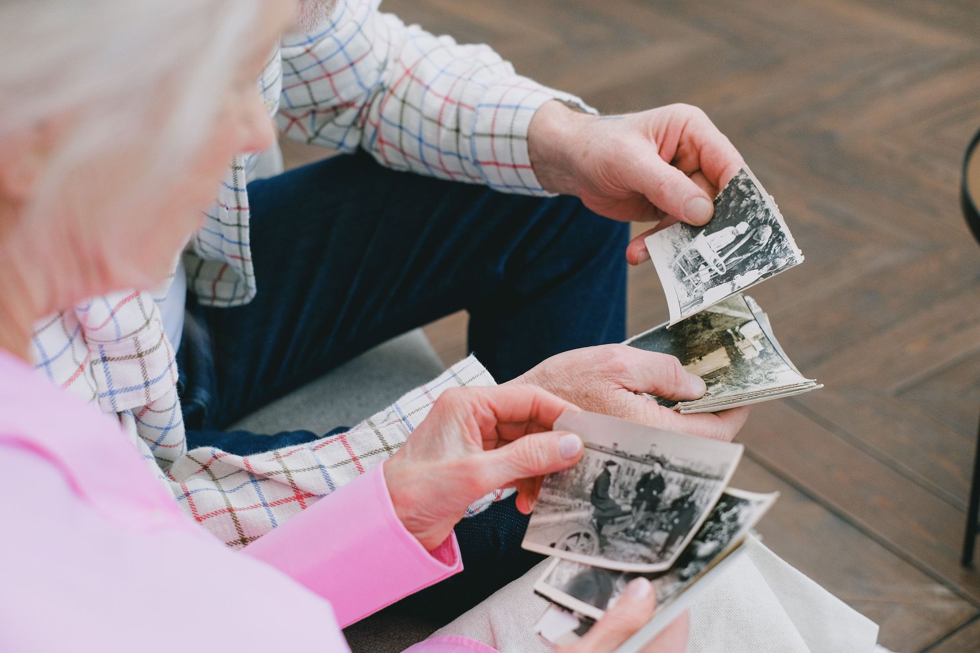 Hands sorting black-and-white photos on a wooden floor beside a pink sleeve