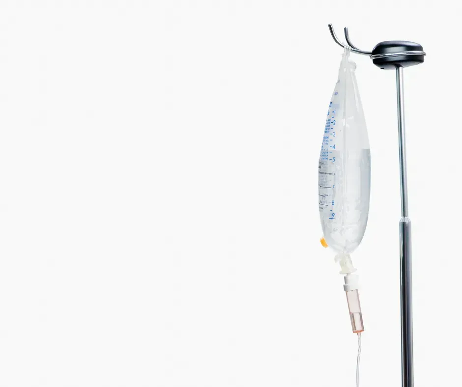 An IV bag filled with fluid hangs from a medical pole against a plain white background.