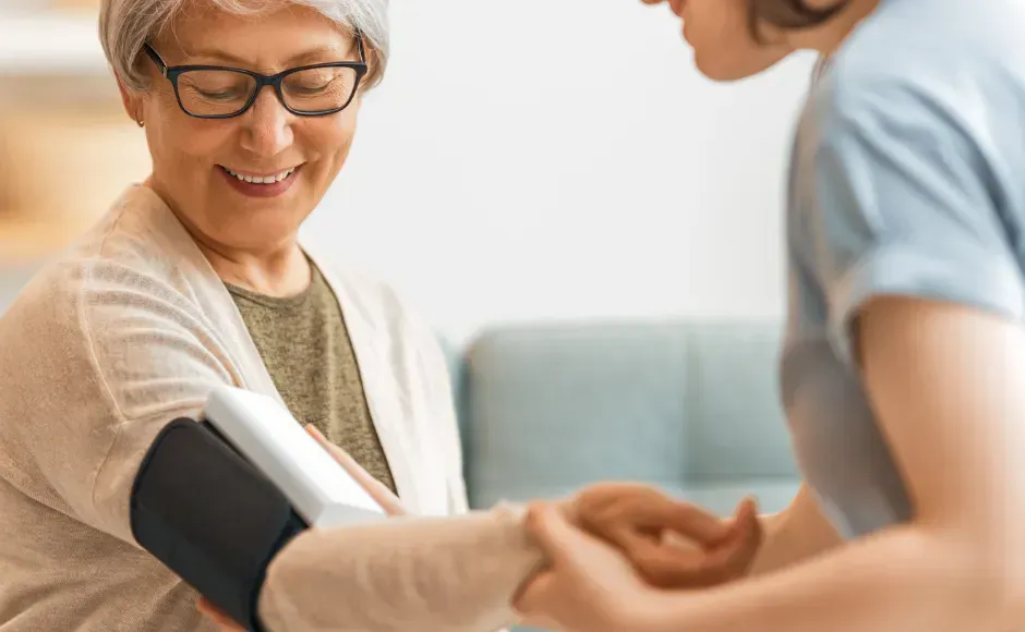 A caregiver assists a person with putting on a digital blood pressure cuff on their upper arm.