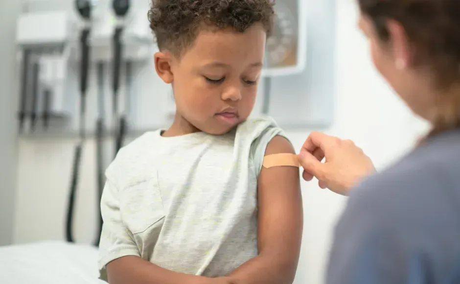 A healthcare worker applies an adhesive bandage to the upper arm of a young person in a medical office.