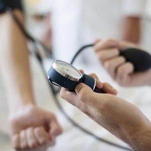 A person measuring another's blood pressure using a sphygmomanometer with a manual pump.