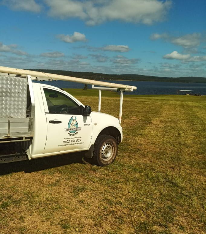 A White Truck is Parked in a Grassy Field Next to a Body of Water — Greg Mitchell Plumbing In Murgon, QLD