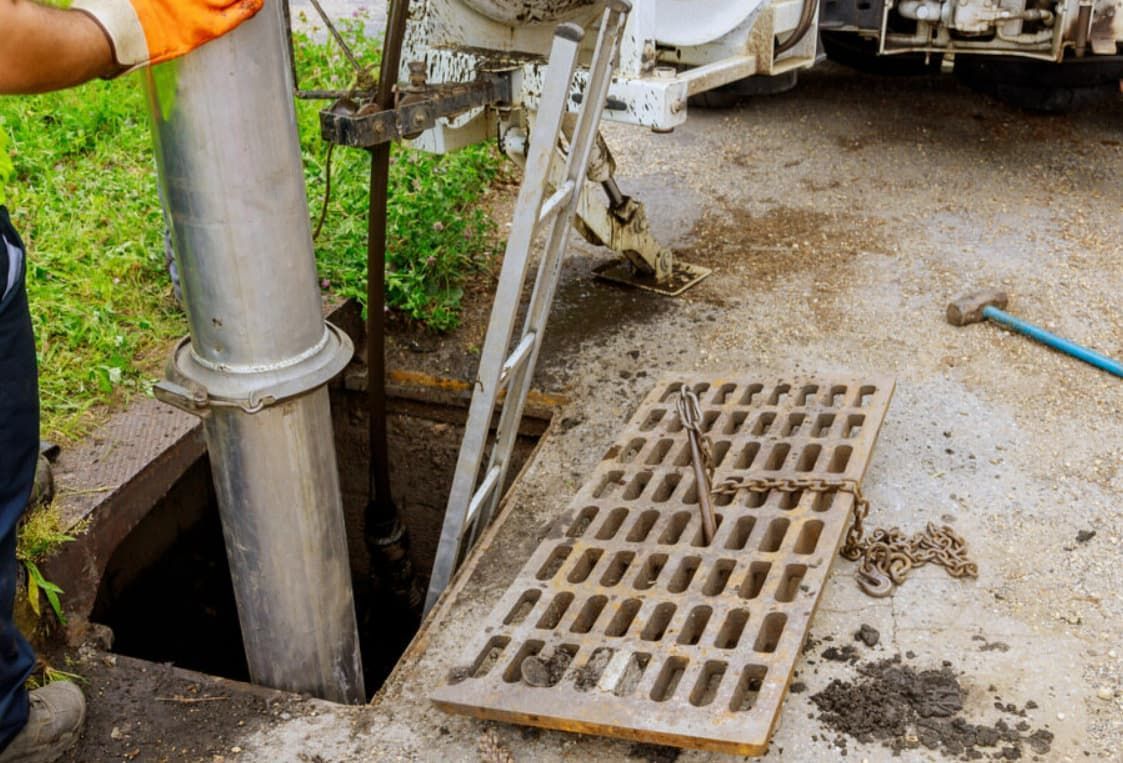 A Man is Working on a Manhole Cover With a Machine — Greg Mitchell Plumbing In Murgon, QLD