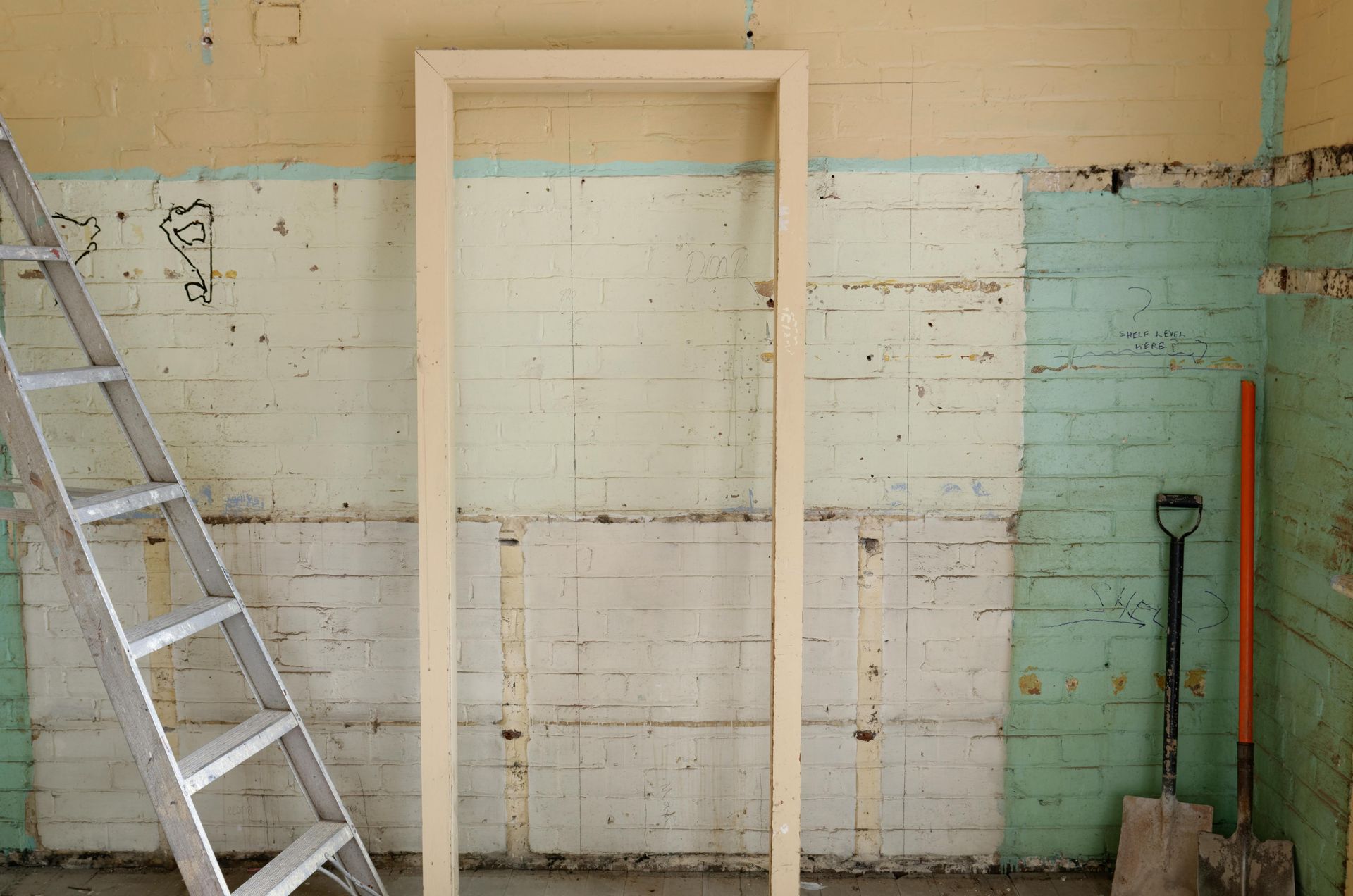Door frame propped against a wall in a room under construction with a ladder and shovel.