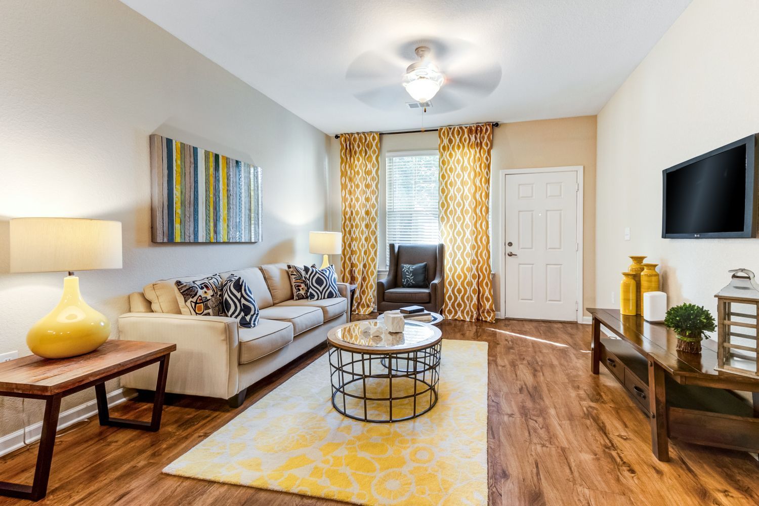 Living room with beige sofa, yellow rug, art, and TV on the wall at The Preserve at Essex Farms, offers apartments in West Charleston, SC.