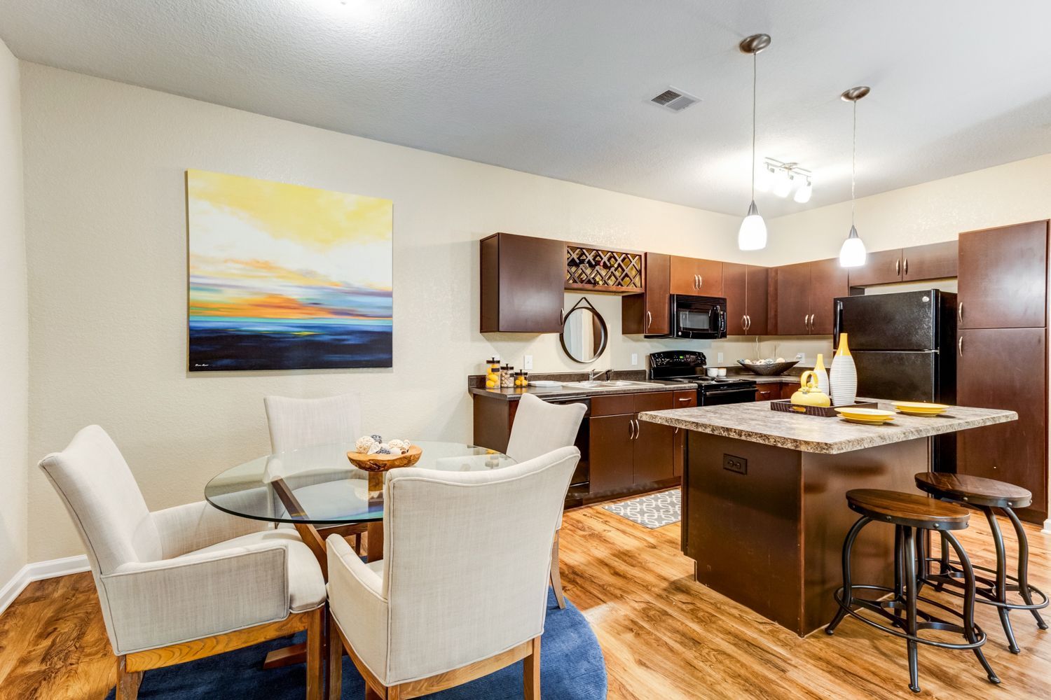 Kitchen and dining area with wood cabinets, island with stools, table with chairs, and artwork at The Preserve at Essex Farms, offers apartments for rent in Charleston, SC.