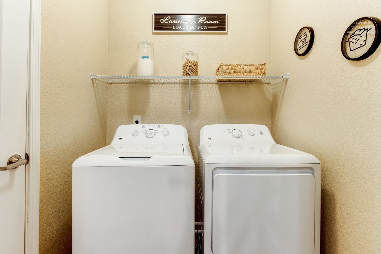 Laundry room with white washer and dryer under a wire shelf with decorations at The Preserve at Essex Farms, offers apartments for rent in West Charleston, SC.
