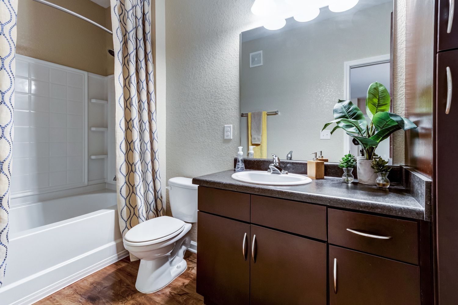 Bathroom with a dark brown vanity, white toilet, and shower with a patterned curtain at The Preserve at Essex Farms, offers apartments for rent in West Charleston, SC.