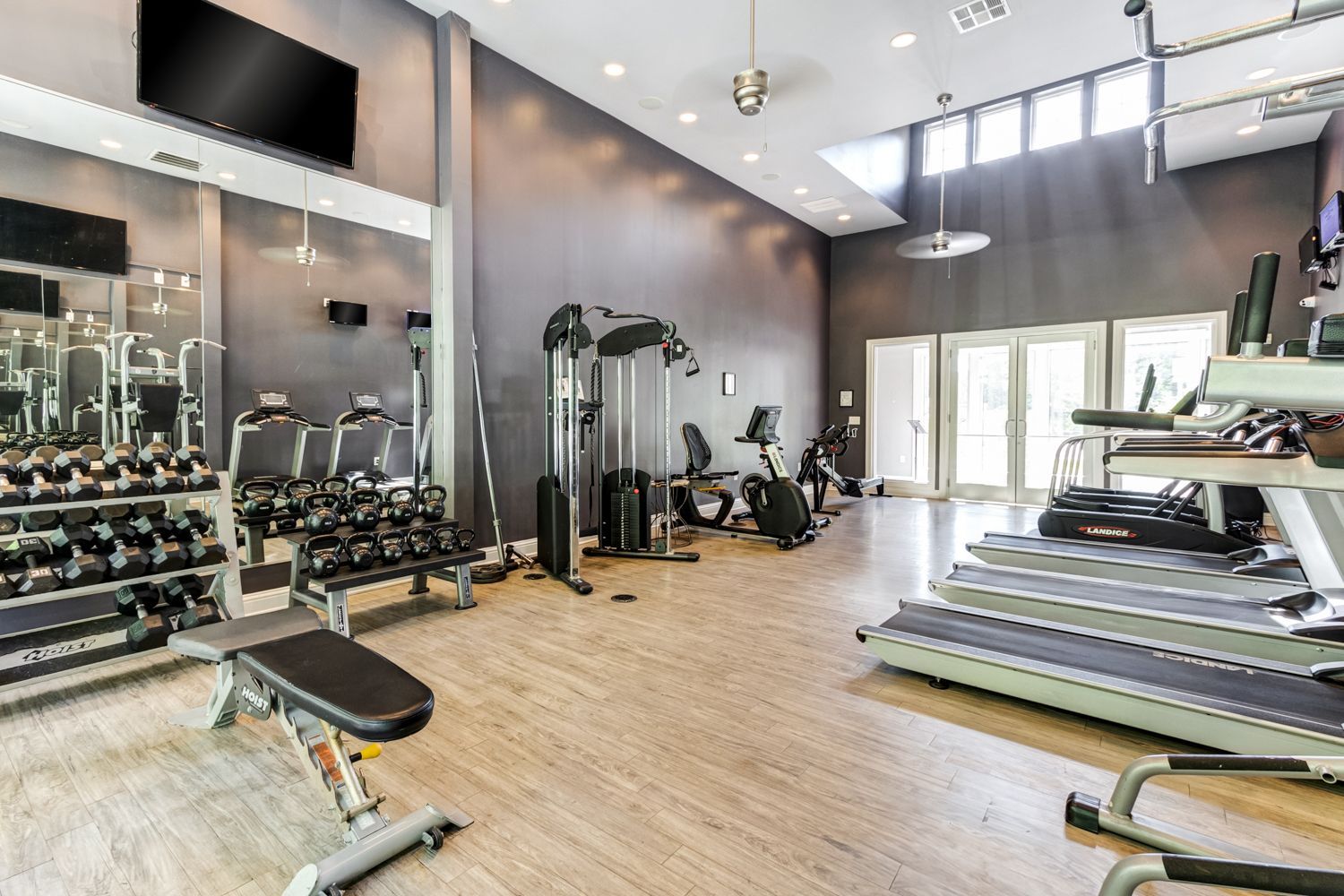 Gym interior with weights, machines, and treadmills; light wood floor, gray walls, windows at The Preserve at Essex Farms, offers pet-friendly apartments in Charleston, SC.