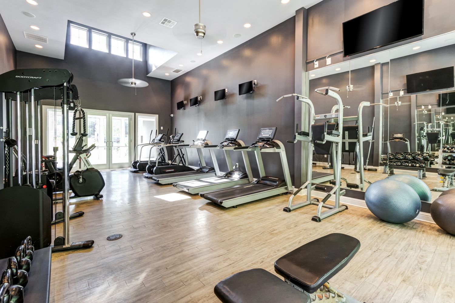 Gym with treadmills, weights, and exercise equipment at The Preserve at Essex Farms, offers pet-friendly apartments in Charleston, SC. Gray walls, wood floors, and large mirrors.