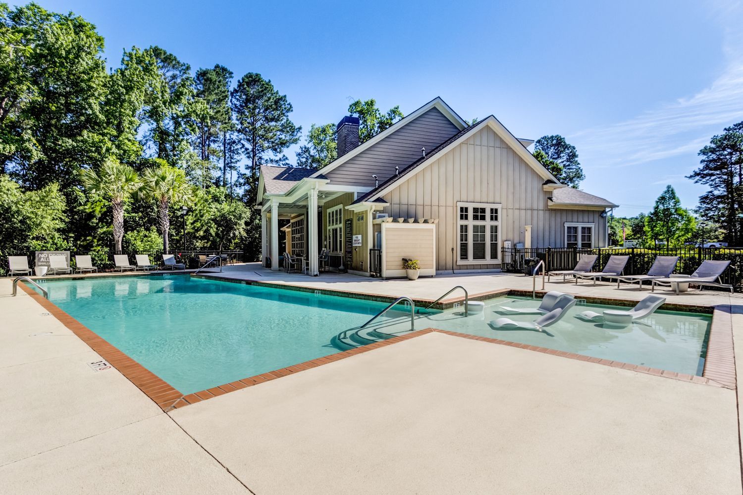Swimming pool with lounge chairs, next to a building with a covered porch and trees at The Preserve at Essex Farms, offers 1, 2, and 3 bedroom apartments in Charleston, SC.