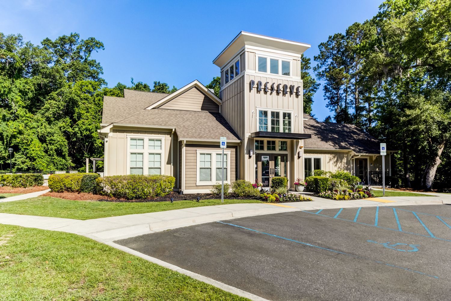 Apartment building with tower, tan and gray exterior, blue parking spaces, sunny day at The Preserve at Essex Farms, offers apartments in West Charleston, SC.