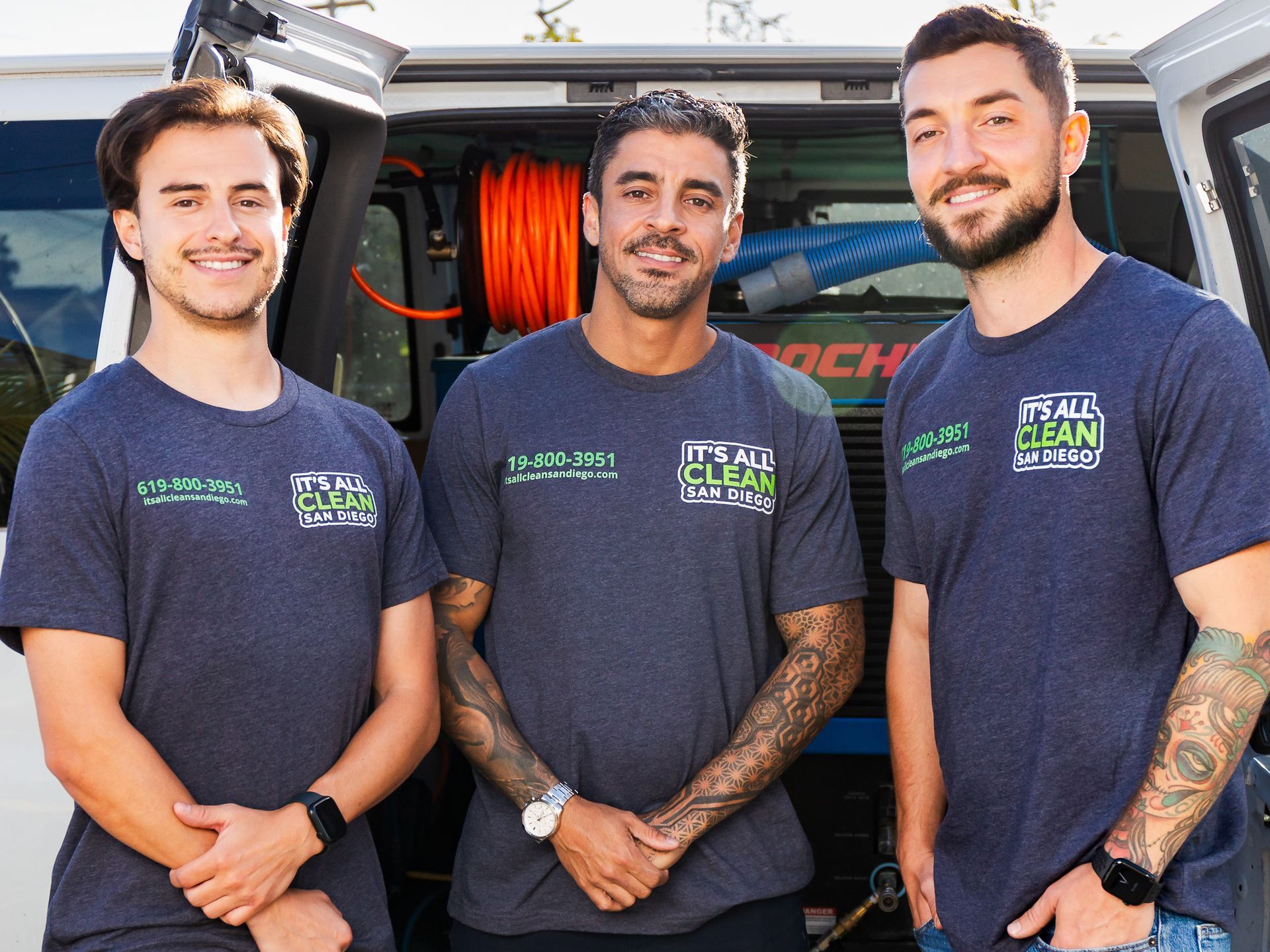 Three men in matching shirts stand in front of a van. The shirts have a logo and phone number.