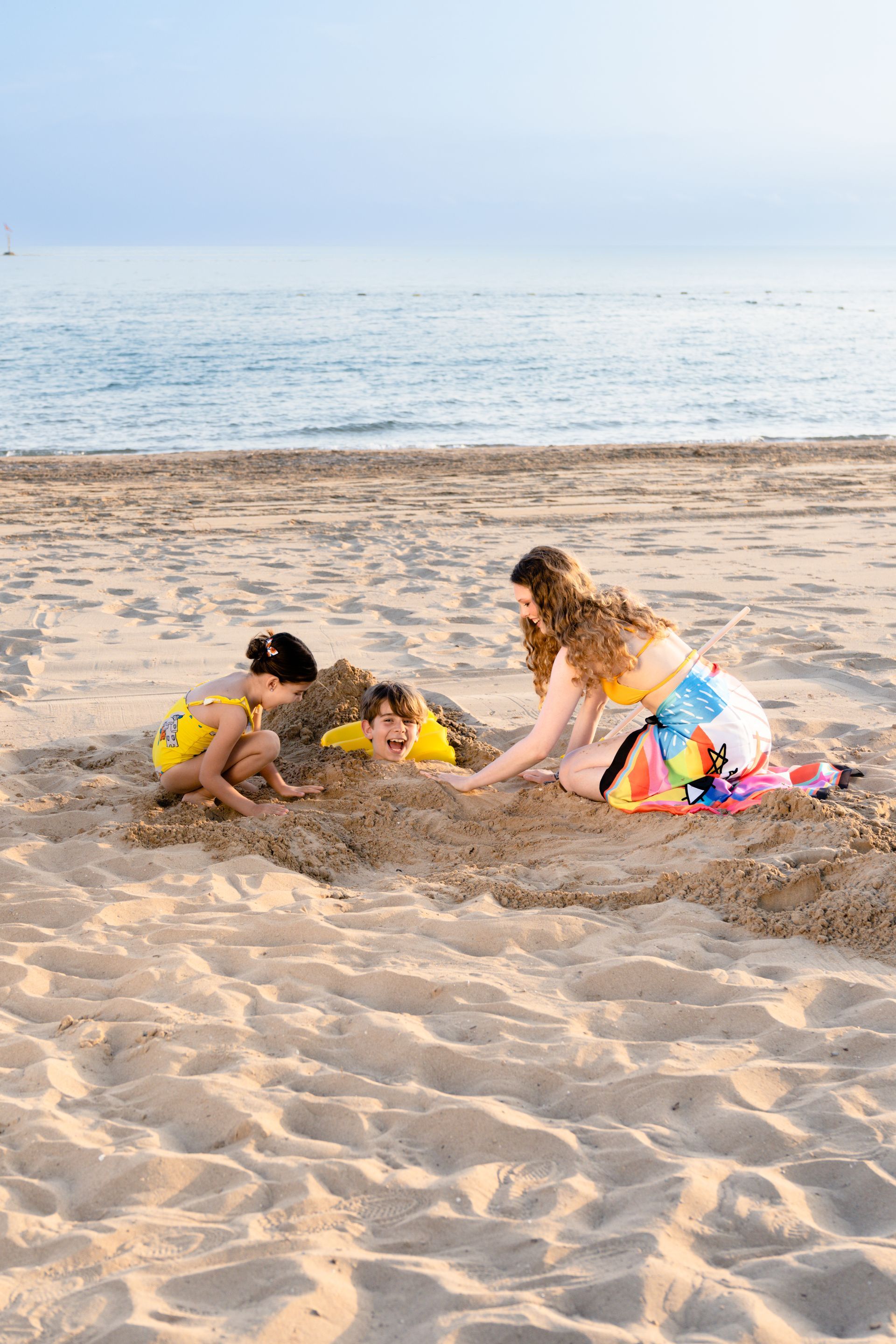 A woman and two children are playing in the sand on the beach.