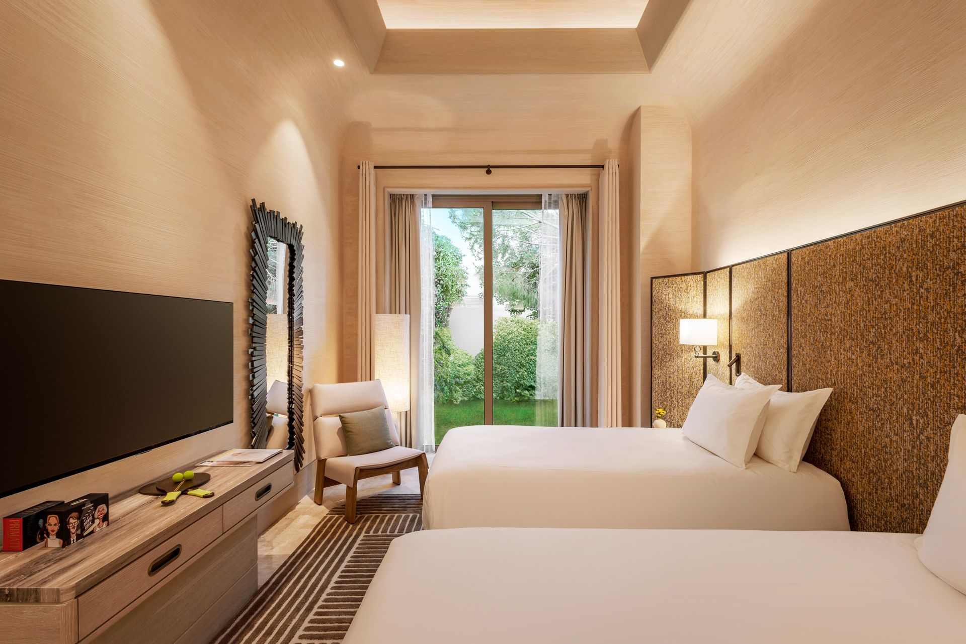 A hotel room with two beds , a chair , a television and a sliding glass door.