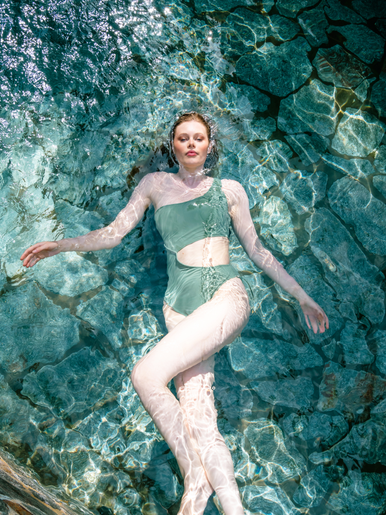 A woman in a green swimsuit is floating in a pool.