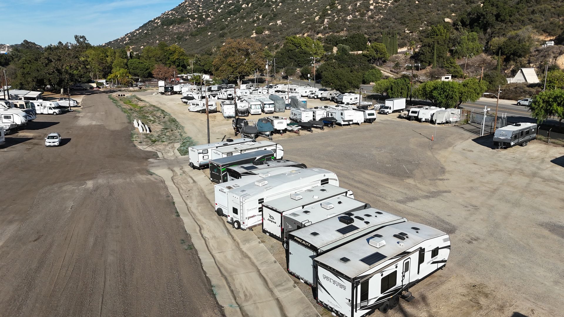 Several white and blue camper trailers parked under a metal frame structure on a gravel lot.