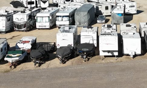Boats stored on racks under a corrugated roof. White and black hulls, blue sky.