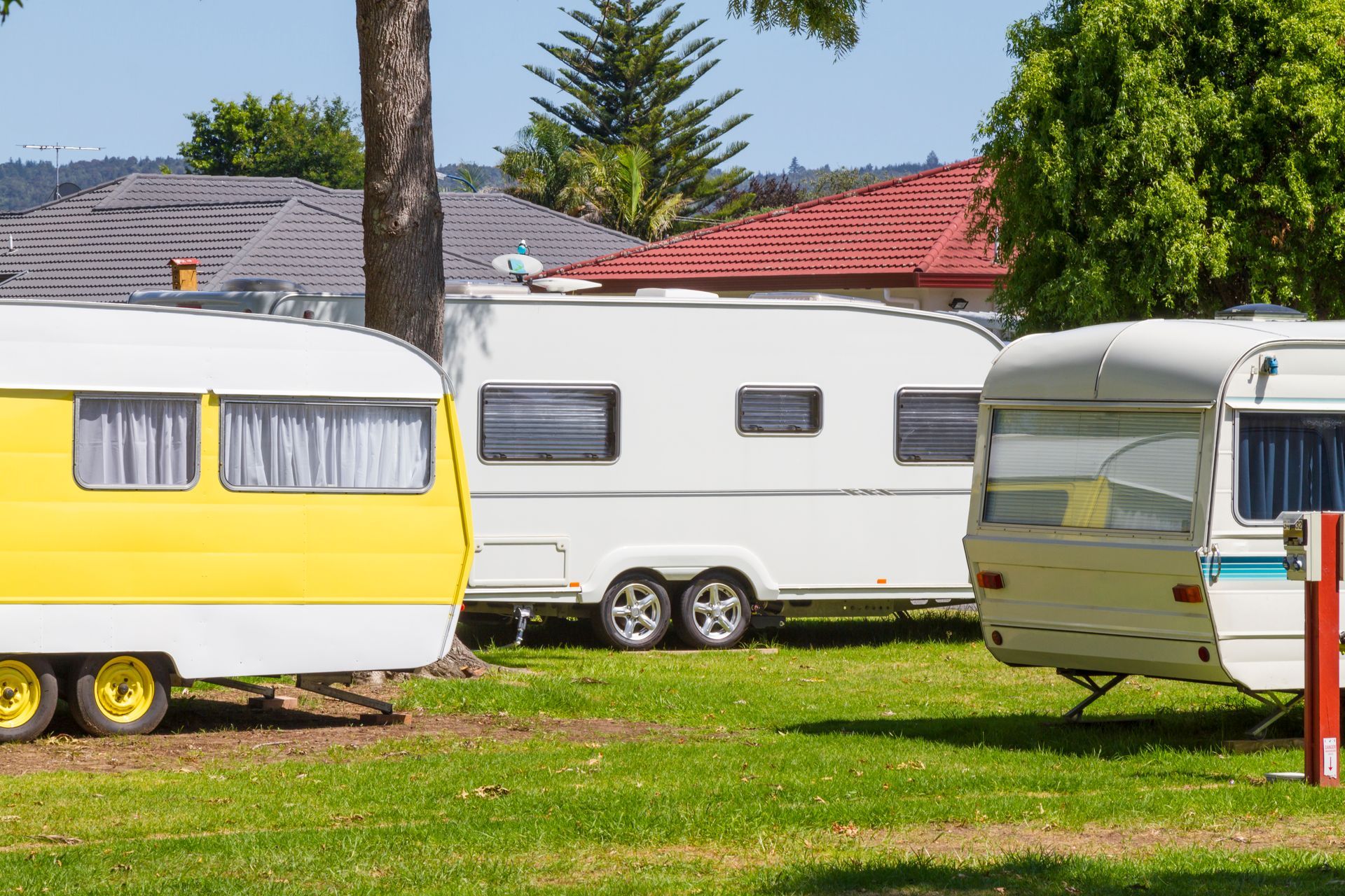 Three colorful camper trailers parked on green grass, houses in background.