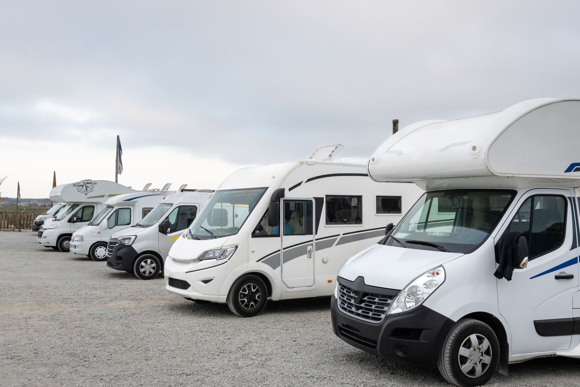 Row of white RVs parked on a gravel lot under a cloudy sky.