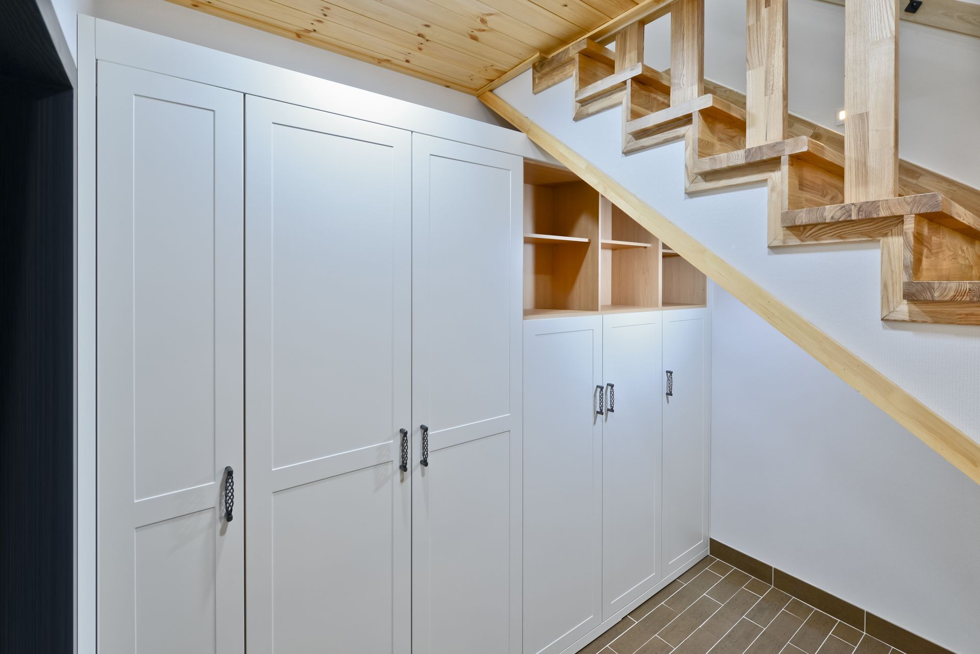 White storage cabinets under wooden staircase; open shelving and dark floor.