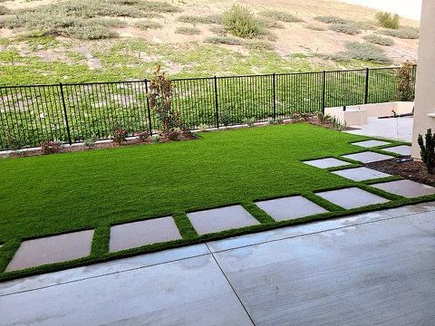 Green lawn with stepping stones and black fence, against a hillside.